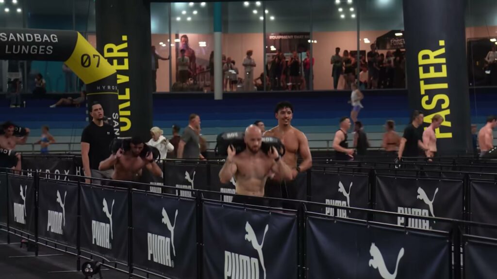 Tom en Ayman doen de sandbag lunges bij HYROX Heerenveen in Thialf, langs borden van PUMA